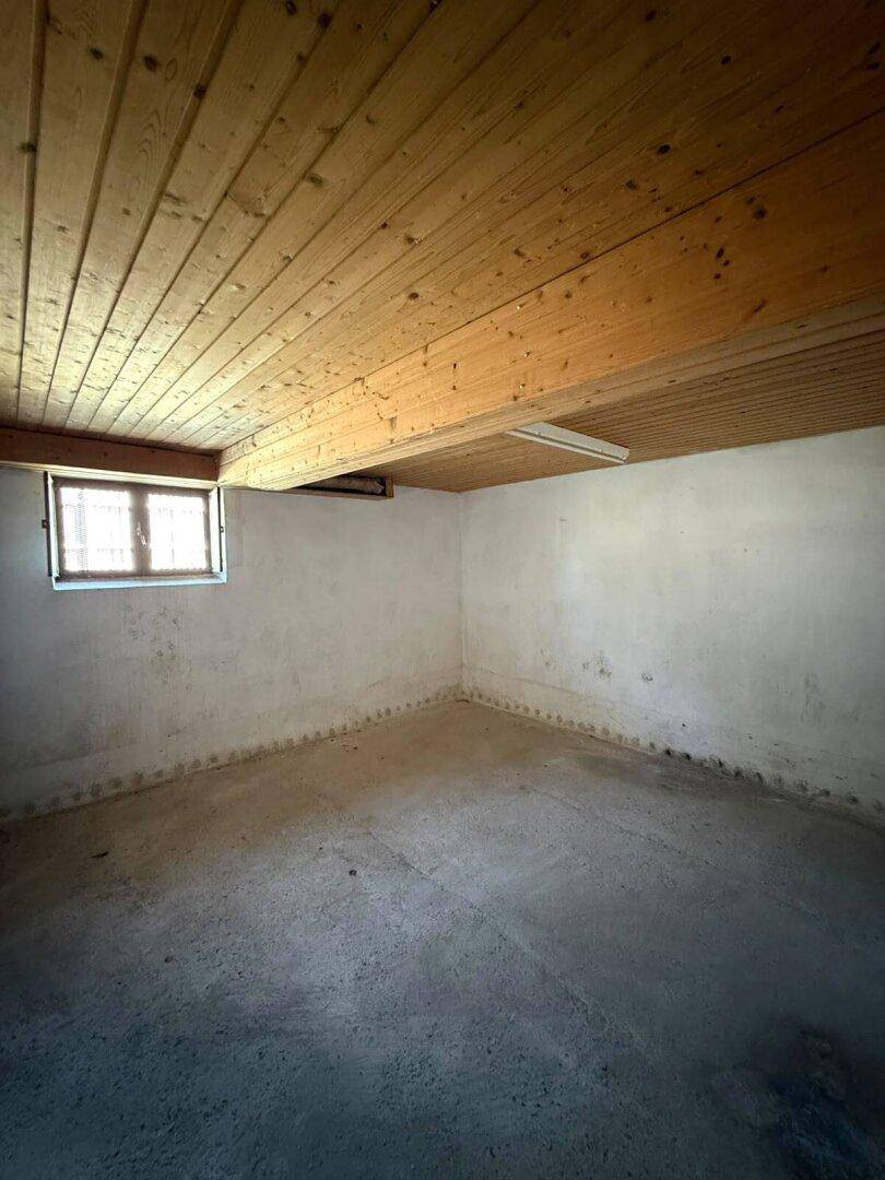 Kellerraum mit Holzdecke, Betonboden und kleinem Fenster, geeignet als Abstellraum.