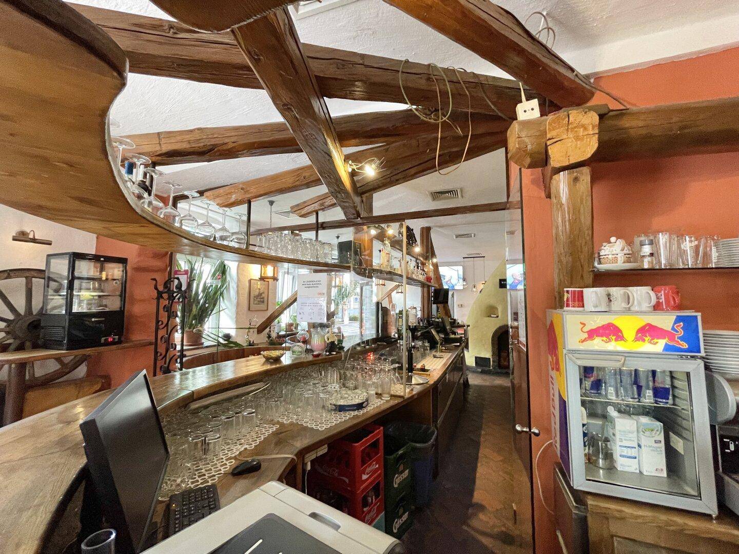 Langer Barbereich mit vielen Gläsern, einer Holztheke und Blick auf den Gastraum mit dem markanten Kamin.