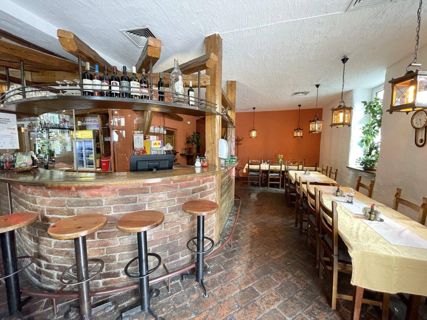 Rustikaler Restaurantbereich mit einer gemauerten Bar, Holztischen und traditionellen Laternen als Beleuchtung.