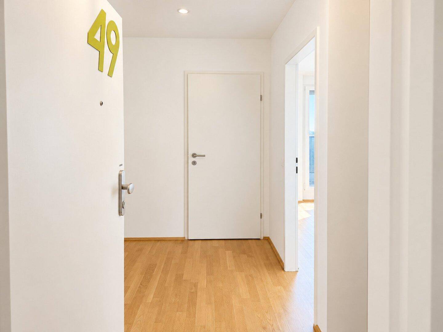 Heller Eingangsbereich mit Parkettboden und der Wohnungsnummer 49 an der Tür.