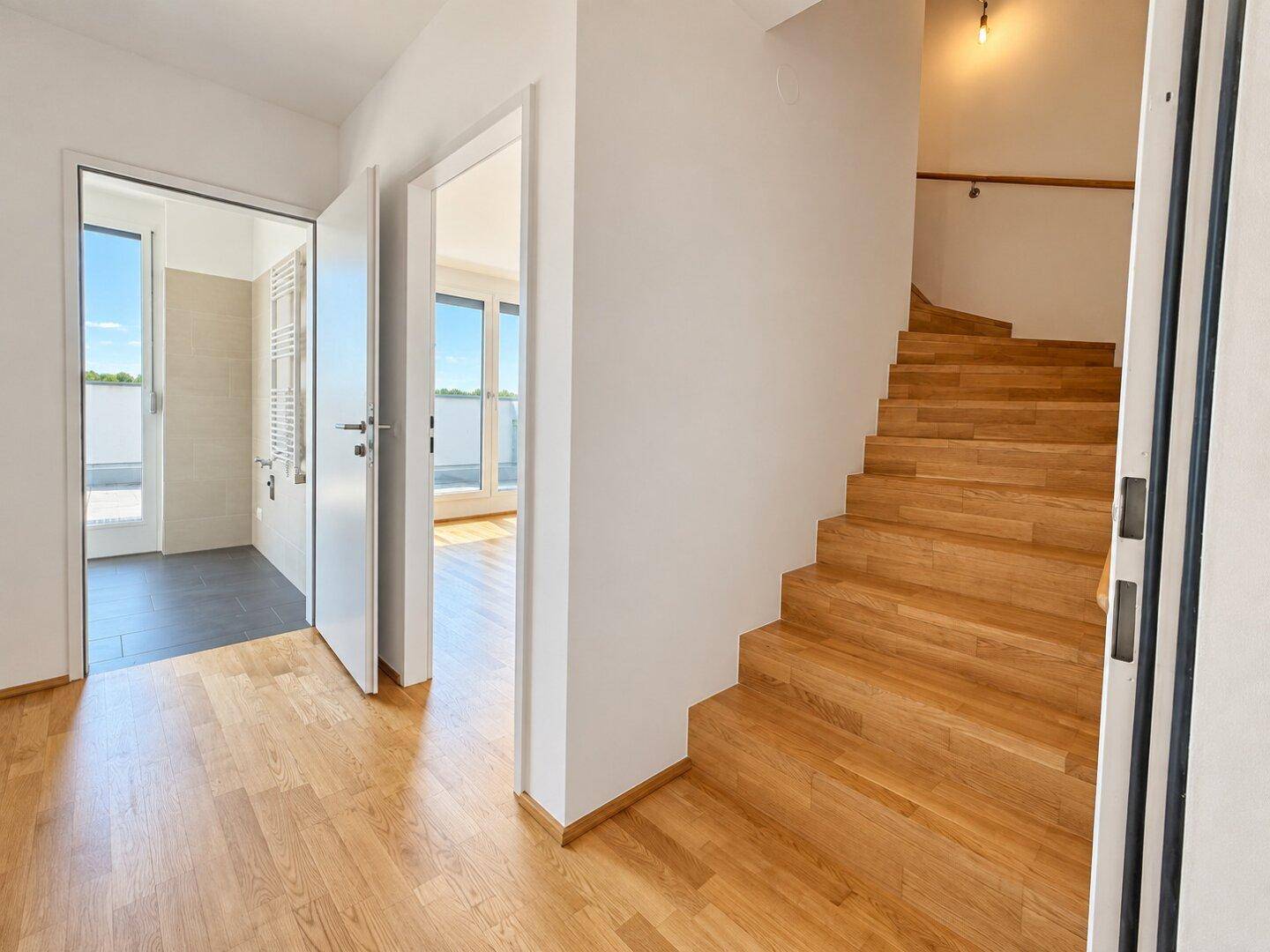 Heller Flur mit Holztreppe und Zugang zu weiteren Räumen und einem Badezimmer.