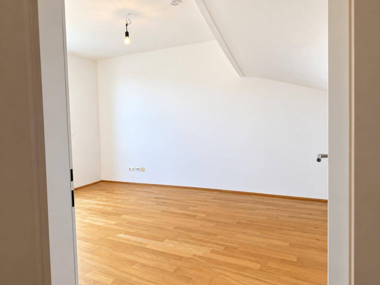 Helles Schlafzimmer im Dachgeschoss mit Parkettboden und schrägen Wänden.