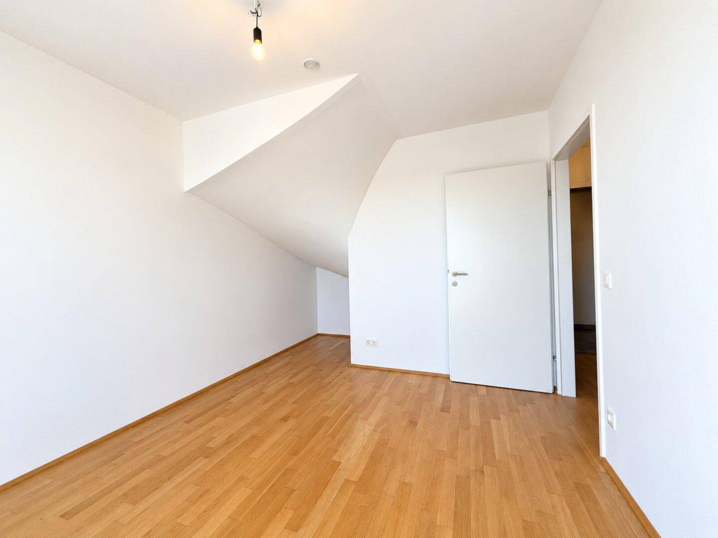 Geräumiges Schlafzimmer mit Parkettboden, weißen Wänden und Dachschrägen.