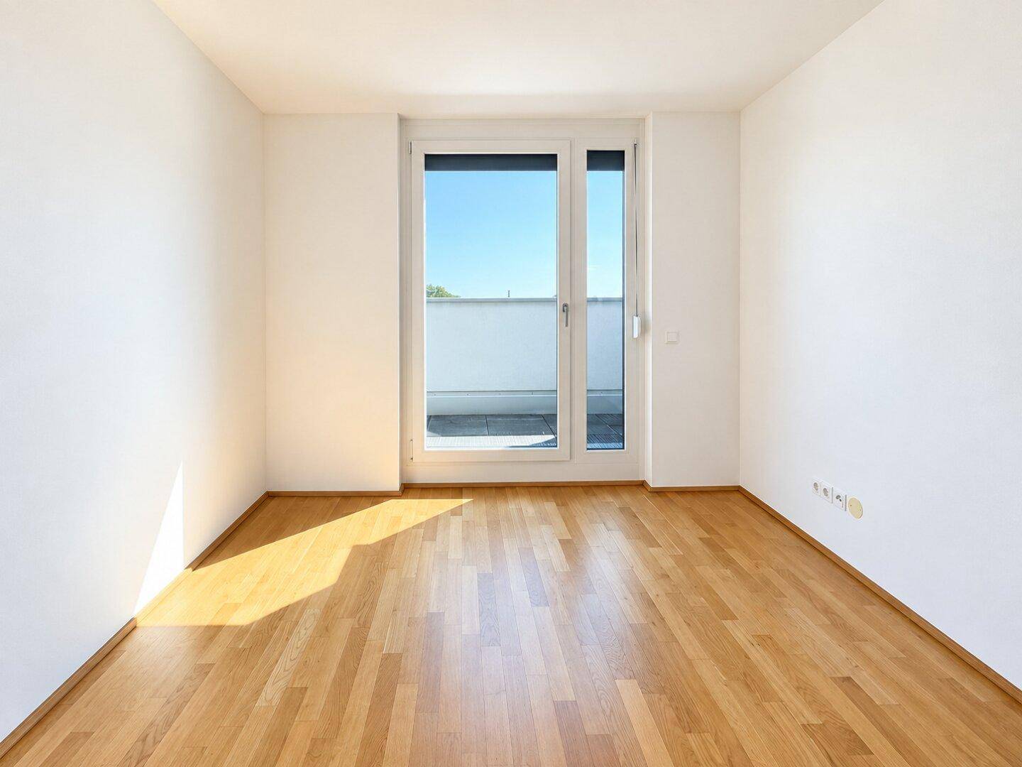 Helles Zimmer mit Parkettboden und großen Fenstern, die auf einen Balkon führen.
