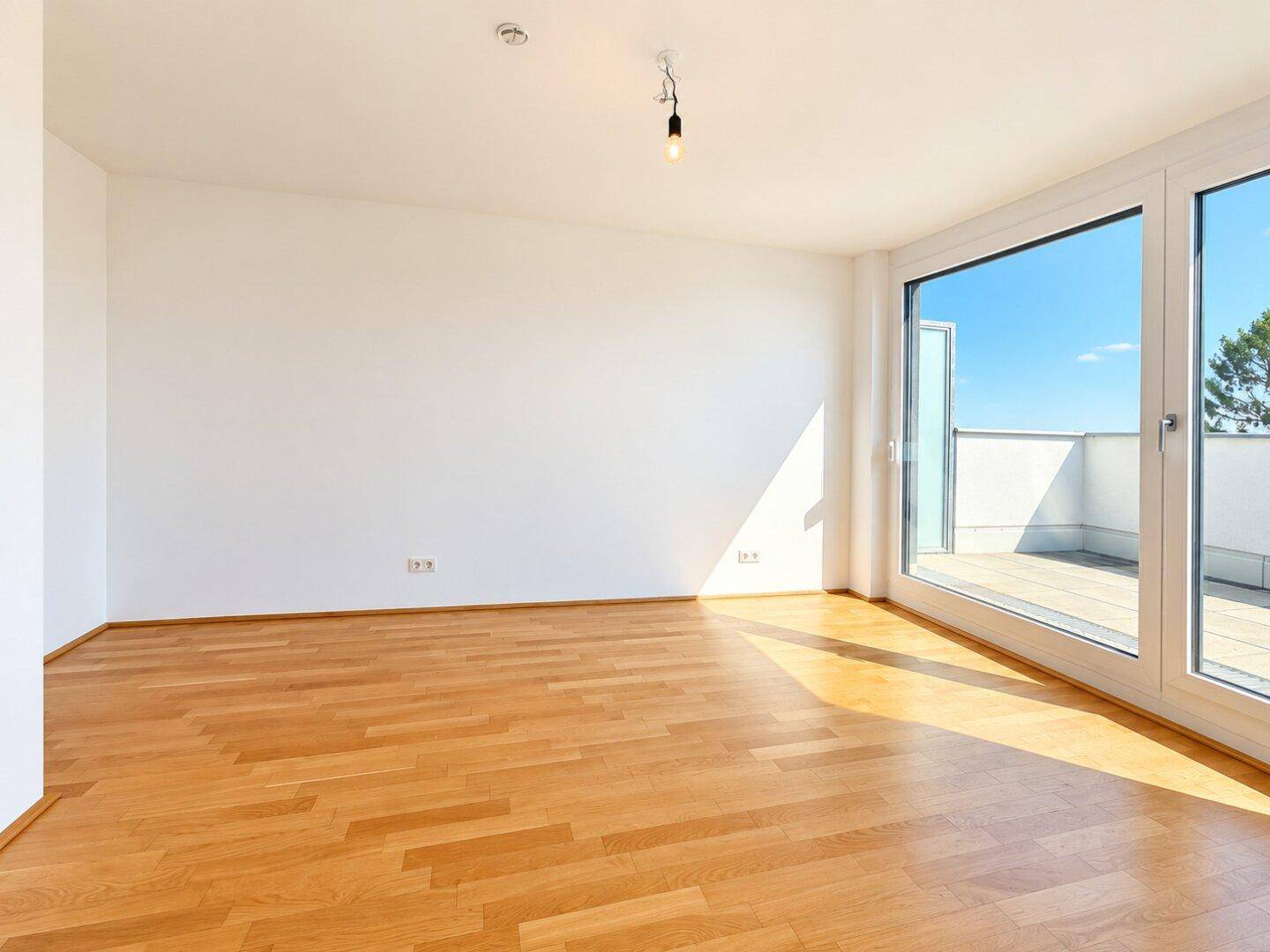 Helles, leeres Zimmer mit Parkettboden und großen Fenstern mit Zugang zur Terrasse.