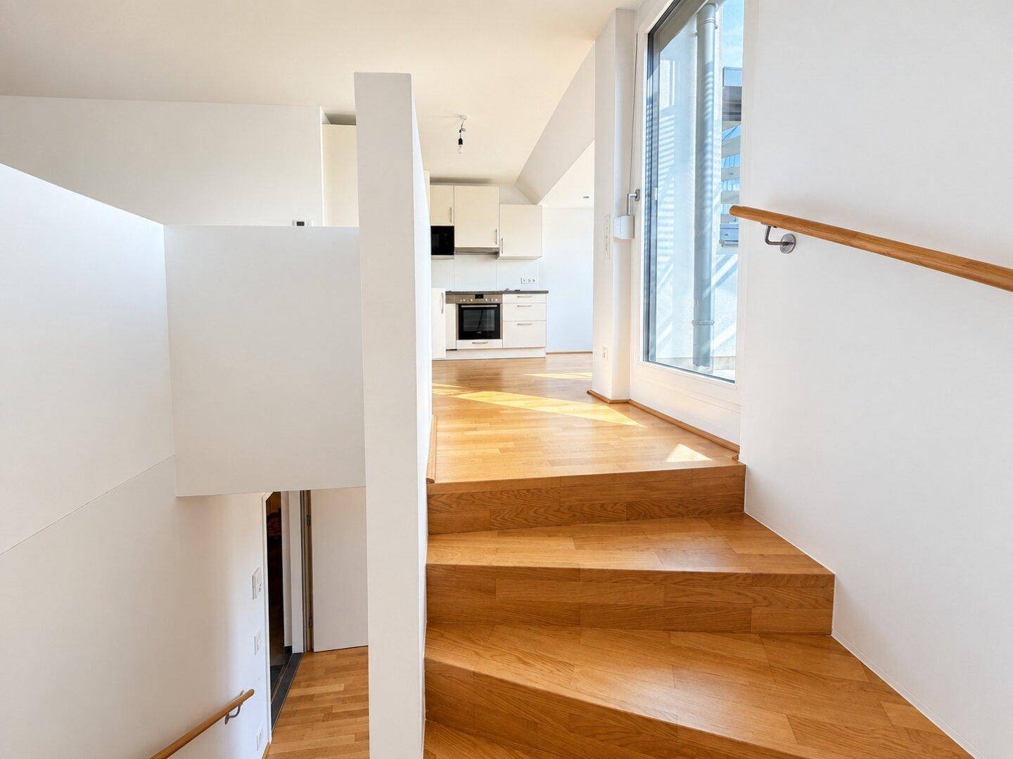 Offener Wohnbereich mit Holztreppe und Blick auf die integrierte Küche.