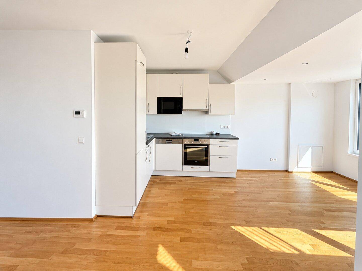Moderne Einbauküche mit weißen Schränken, integrierten Geräten und Parkettboden.
