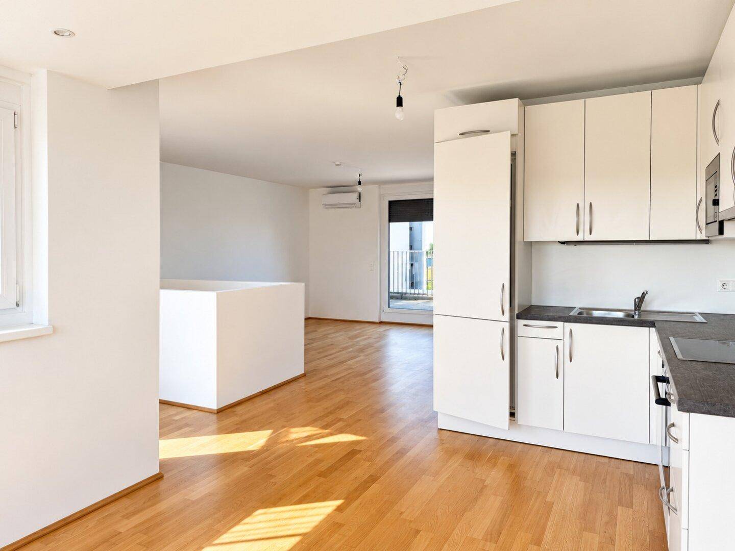 Offener Wohnbereich mit integrierter Küche, Parkettboden und Zugang zum Balkon.