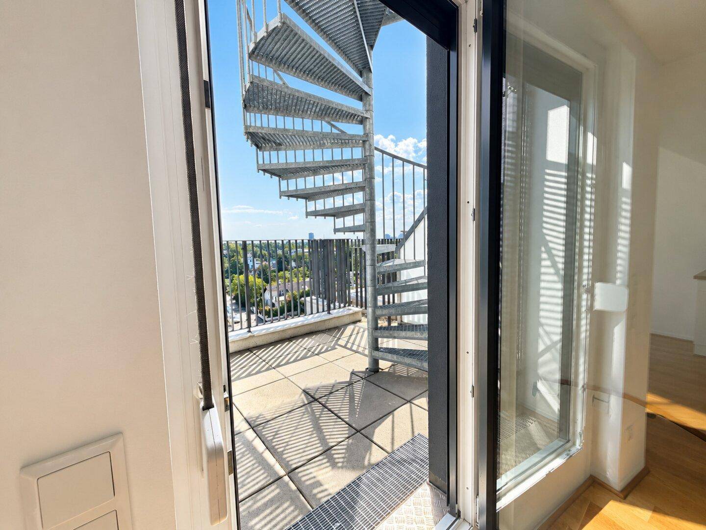 Zugang zu einer Dachterrasse über eine Wendeltreppe mit weitem Stadtblick.