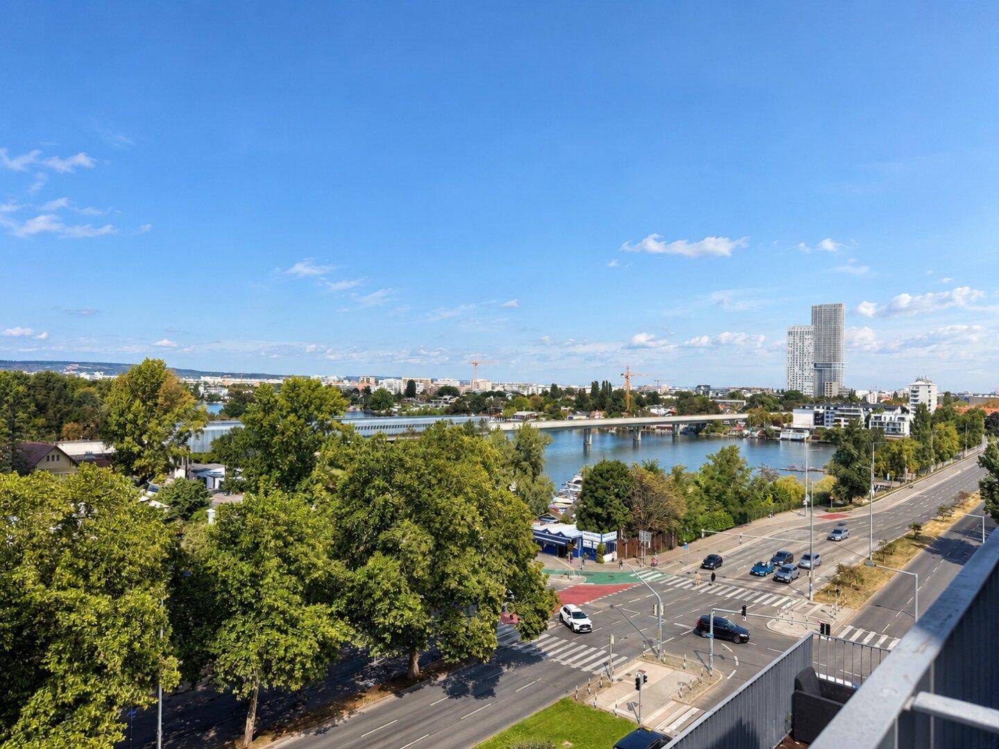 Weitläufiger Blick über eine belebte Straße, einen Fluss mit Brücke und die Skyline einer Stadt am Horizont.