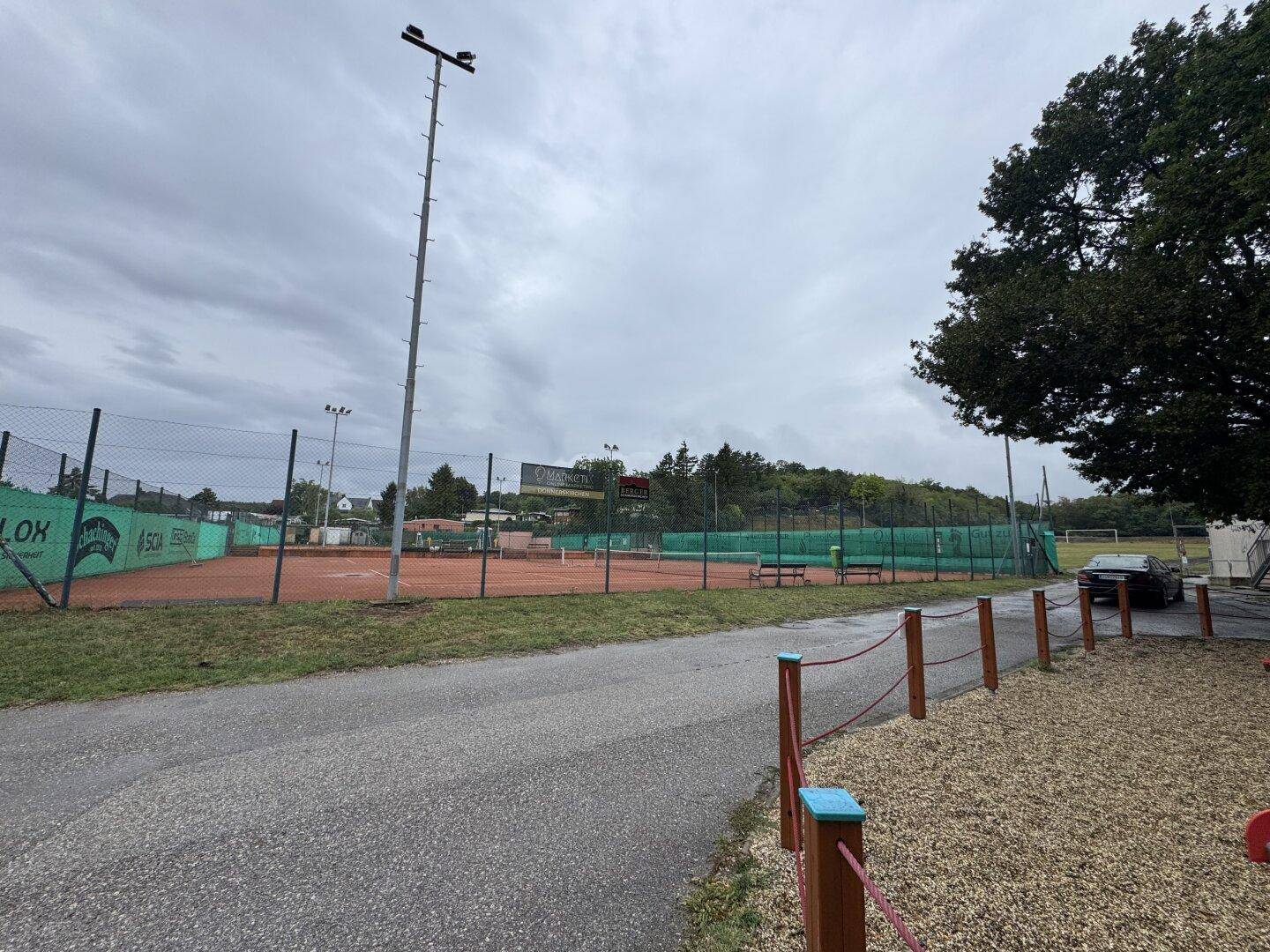 Außenansicht von Tennisplätzen unter bewölktem Himmel, bereit für sportliche Aktivitäten.