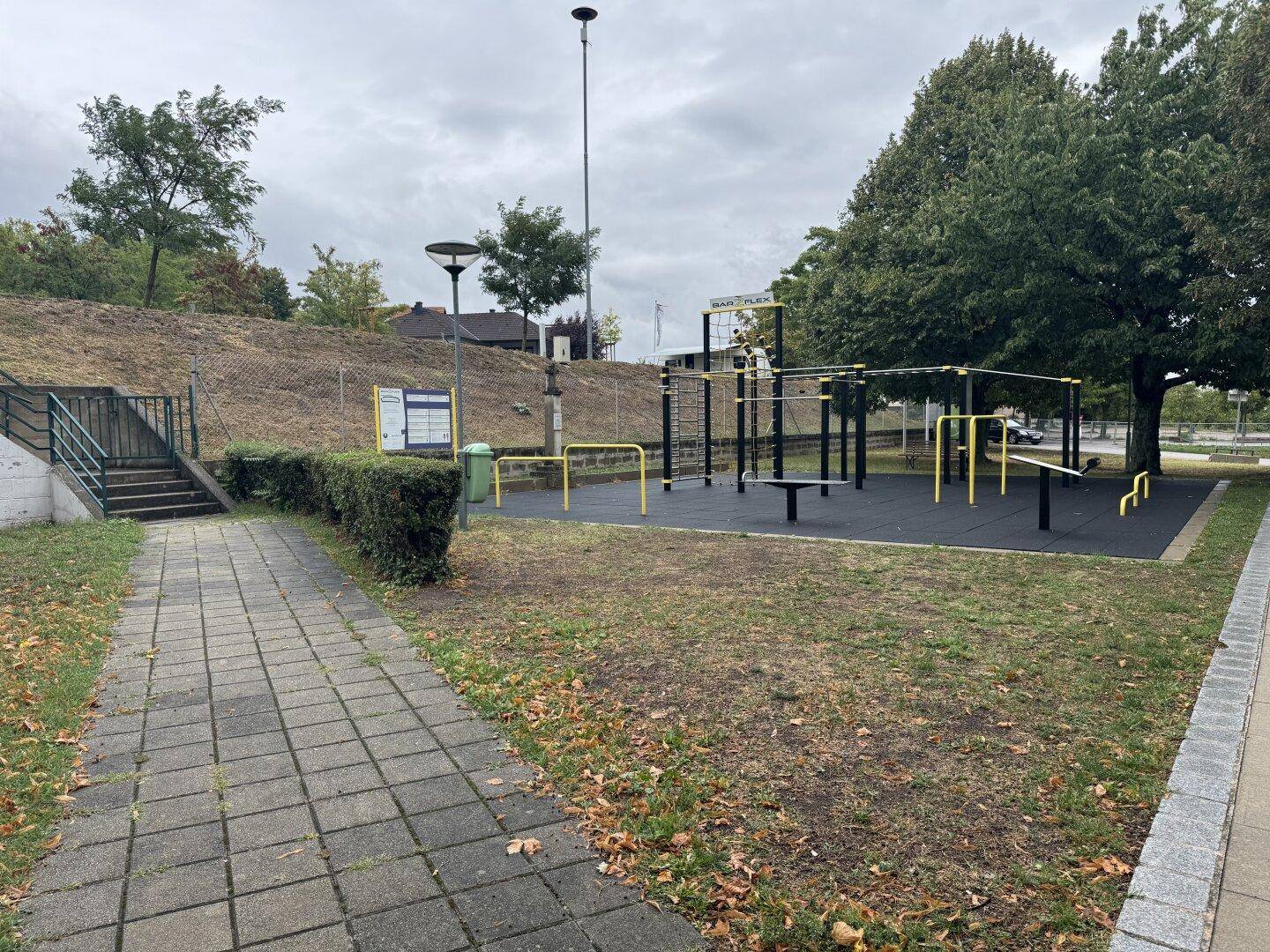 Outdoor-Fitnessbereich mit verschiedenen Geräten und gepflastertem Weg, ideal für Training.