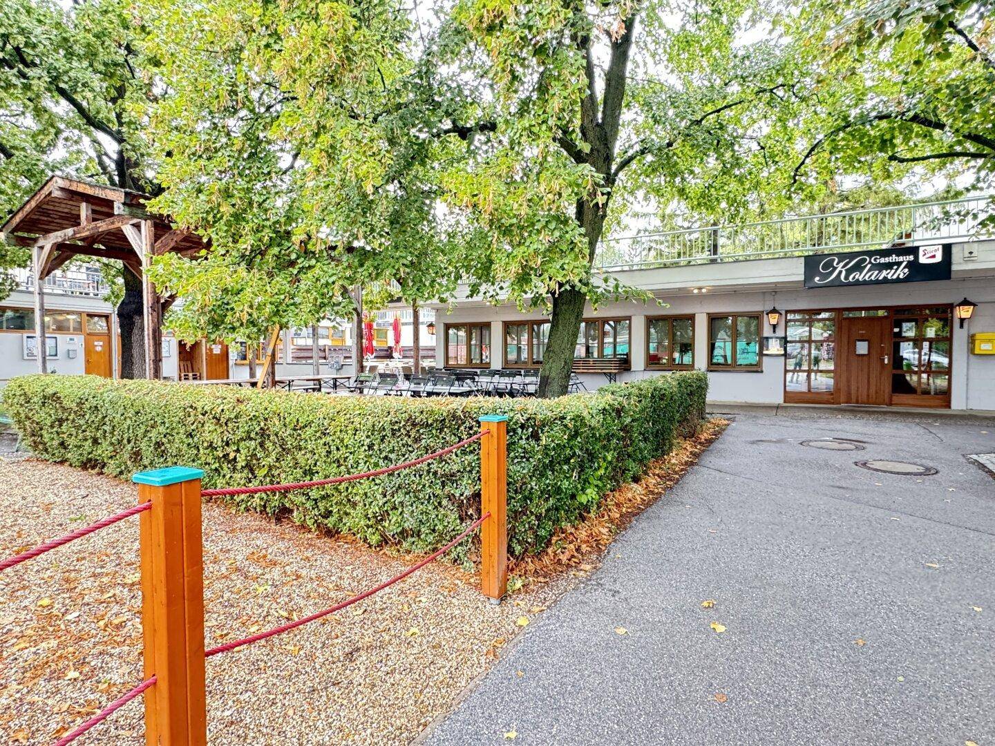 Außenansicht des Gasthauses Kolarik mit Baumbestand und Hecke, einladend für Gäste.