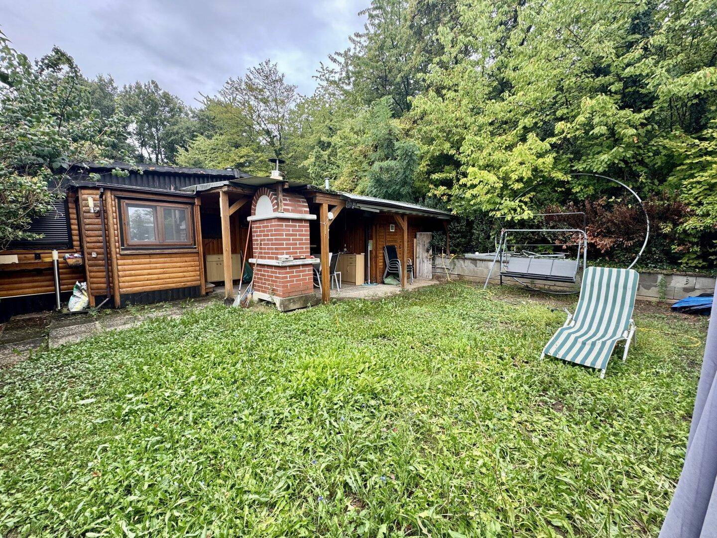 Geräumiger Garten mit Rasenfläche, Holzhaus, Grillplatz und einer Schaukel im Hintergrund.