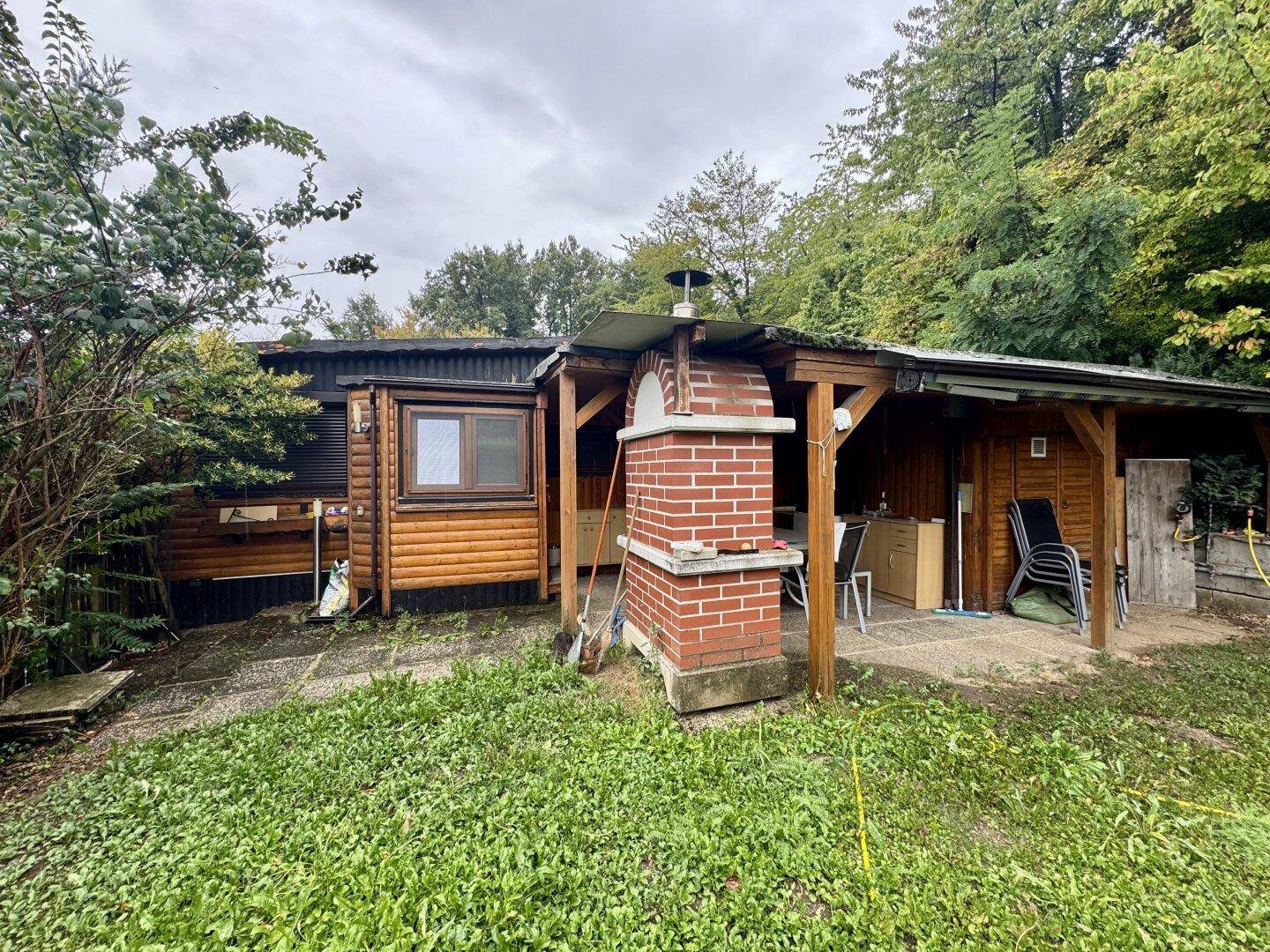 Gartenbereich mit Holzhaus, überdachtem Sitzplatz und gemauertem Grill für gesellige Stunden.
