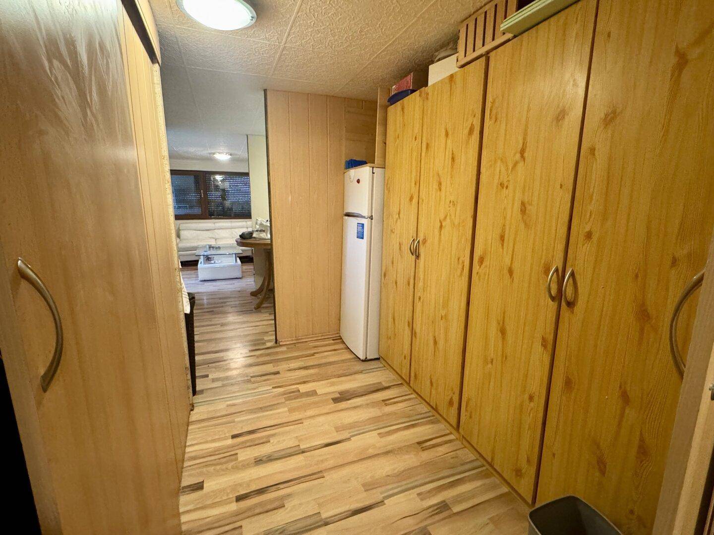 Flur mit Holzschränken und Kühlschrank, der zu weiteren Räumen des Hauses führt.