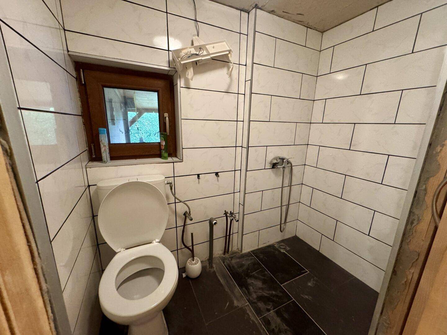 Badezimmer mit WC, Duschbereich und weißen Fliesen an den Wänden, modern und funktional.