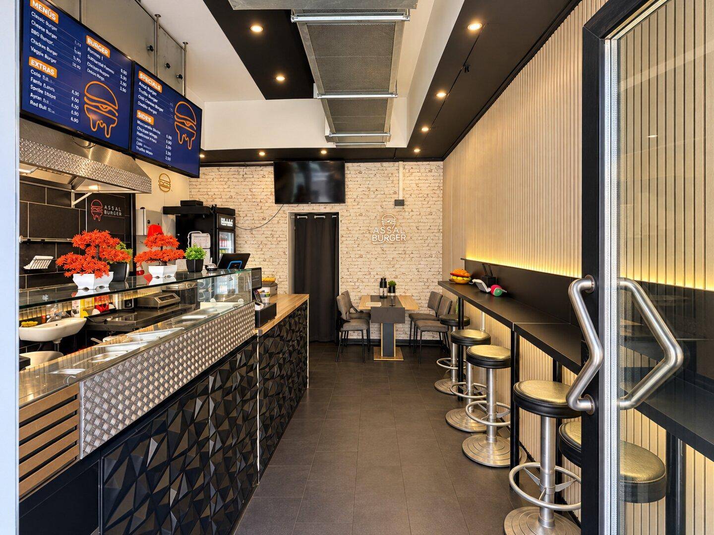 Innenansicht eines modernen Burger-Restaurants mit Theke, Sitzgelegenheiten und Holzwandverkleidung.