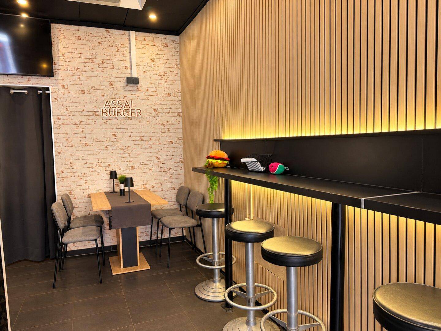 Gemütlicher Sitzbereich in einem Burger-Restaurant mit Holzwand, Bartresen und kleinen Tischen.
