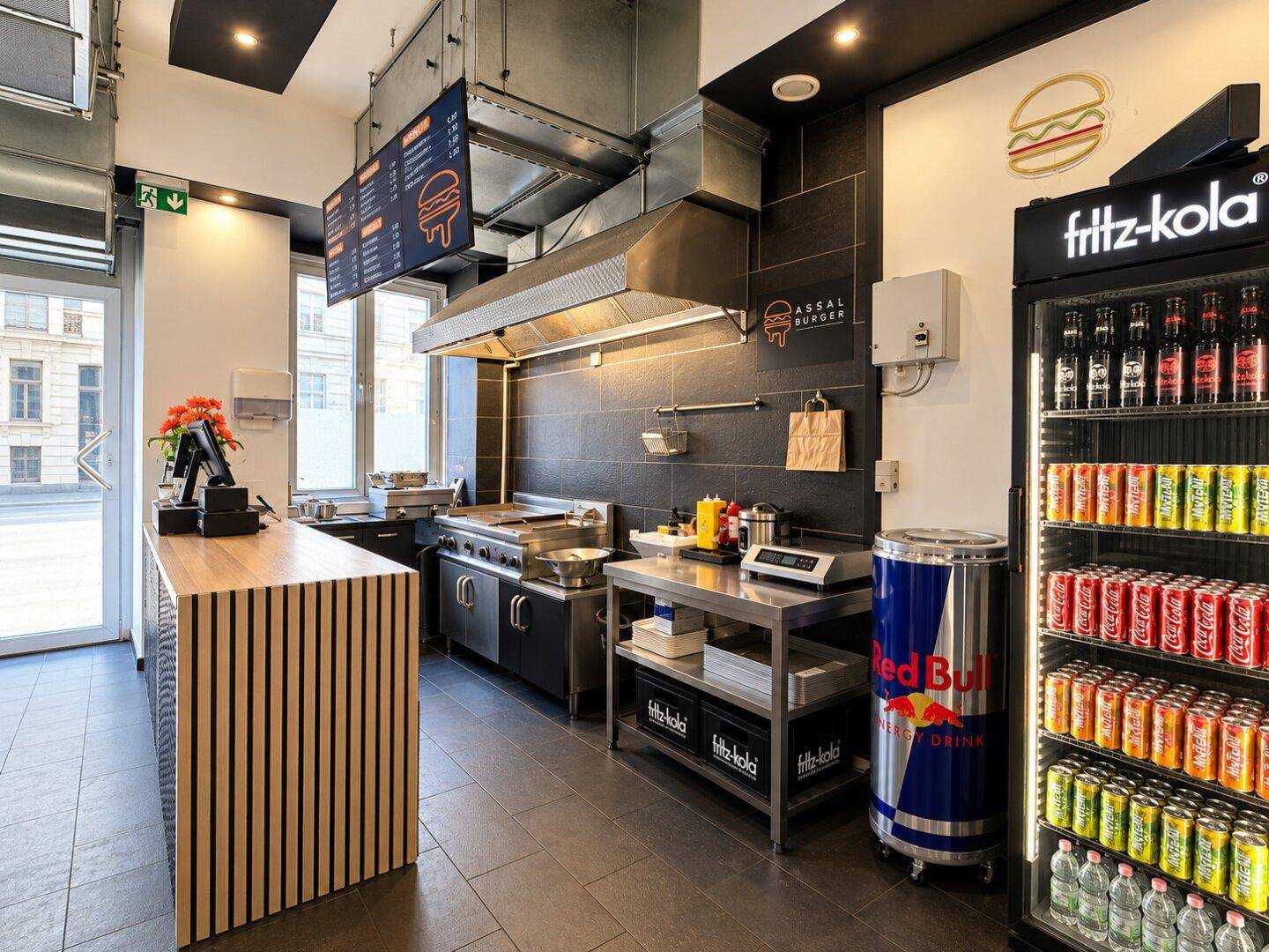 Professionelle Küche eines Burger-Restaurants mit Edelstahlgeräten, Abluftsystem und Getränkekühlschrank.