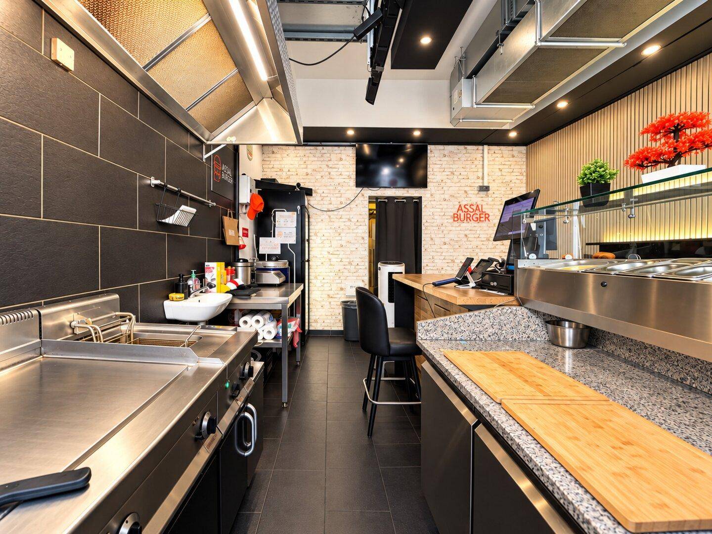 Blick in die professionelle Küche mit Grillstation, Arbeitsflächen und Zugang zum Lagerbereich.