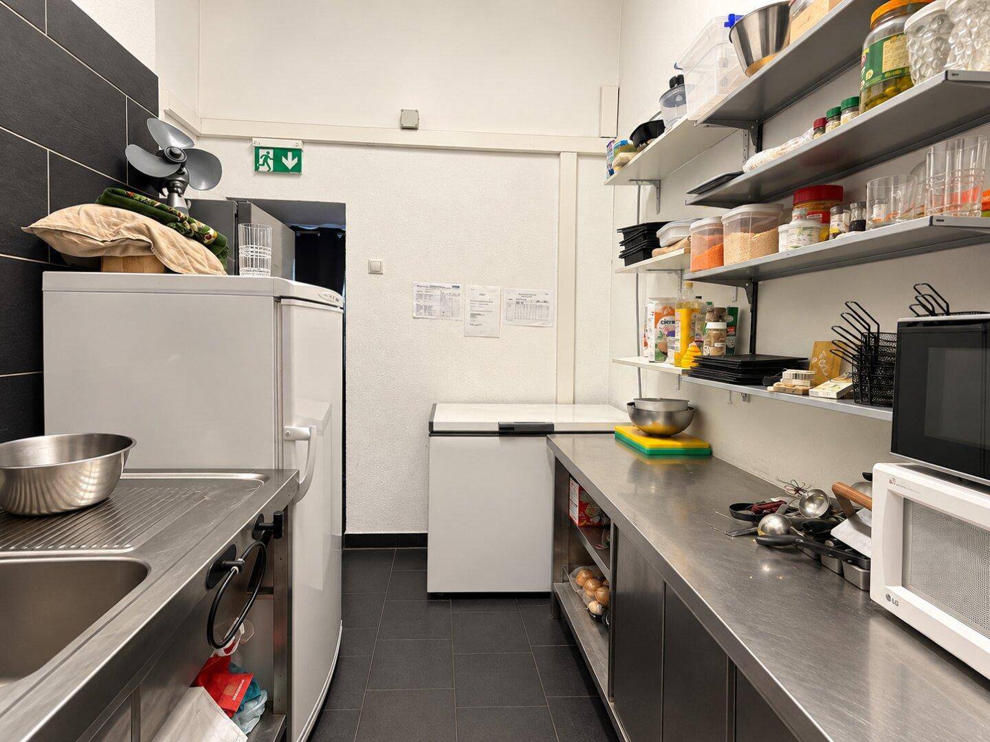 Weiterer Blick in den Lagerraum mit Gefrierschrank, Regalen und Arbeitsflächen aus Edelstahl.