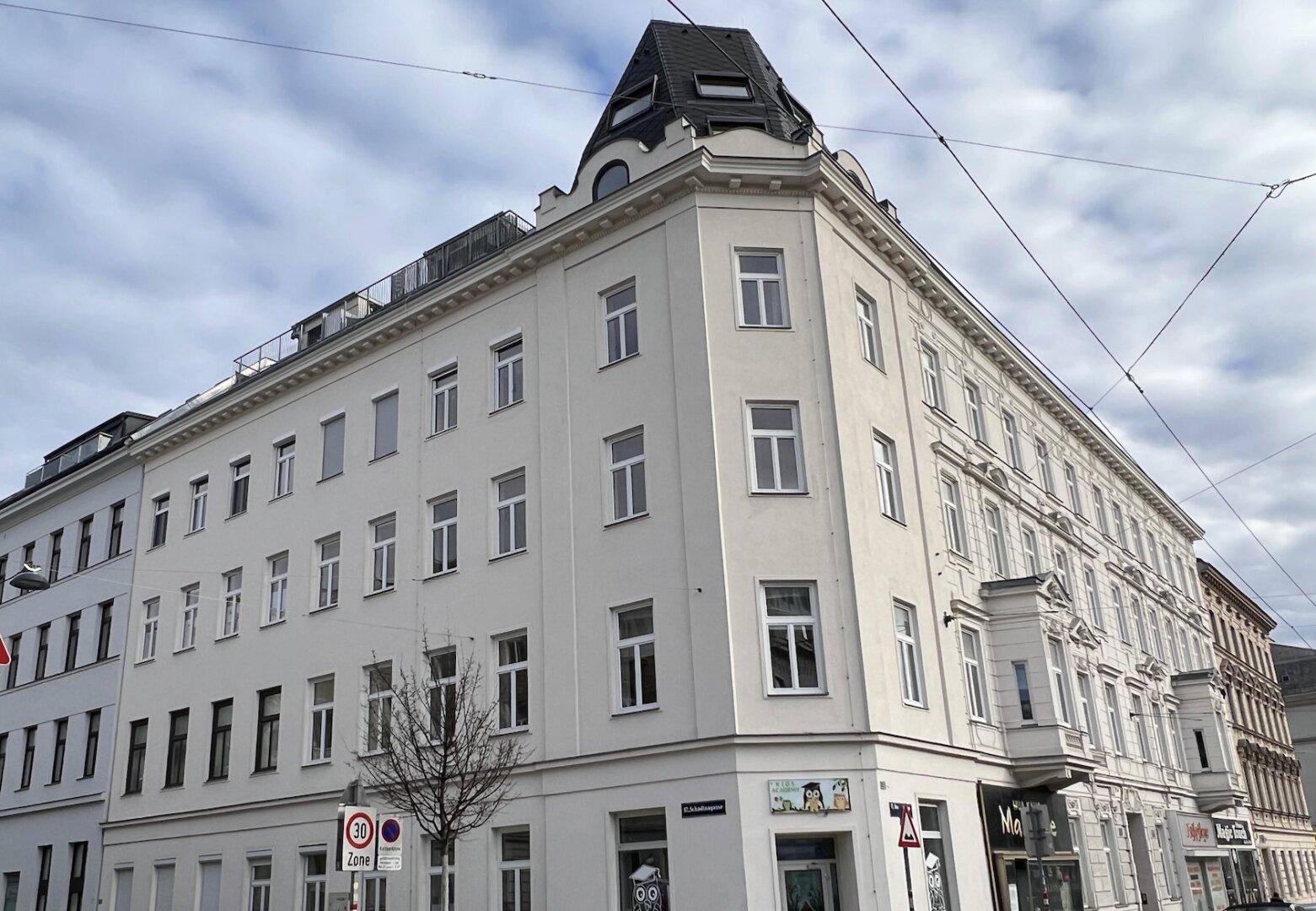 Historisches Eckgebäude mit klassischer Architektur, vielen Fenstern und Mansarddach.