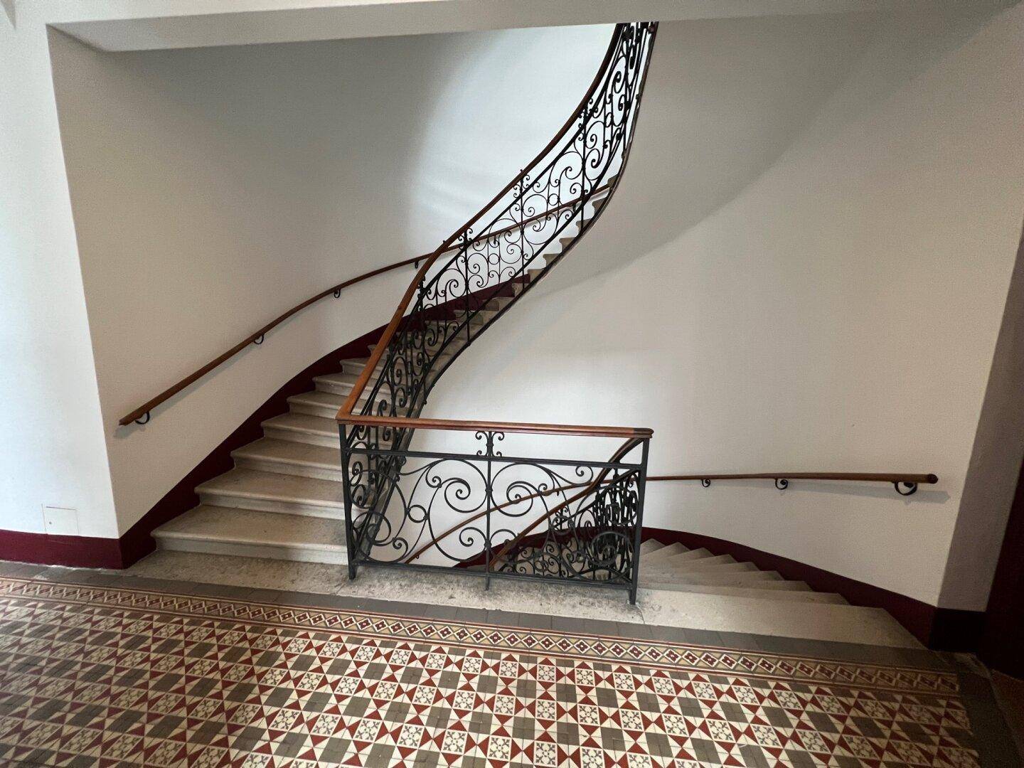 Historisches Treppenhaus mit kunstvollem Geländer und gemustertem Fliesenboden im Altbau.
