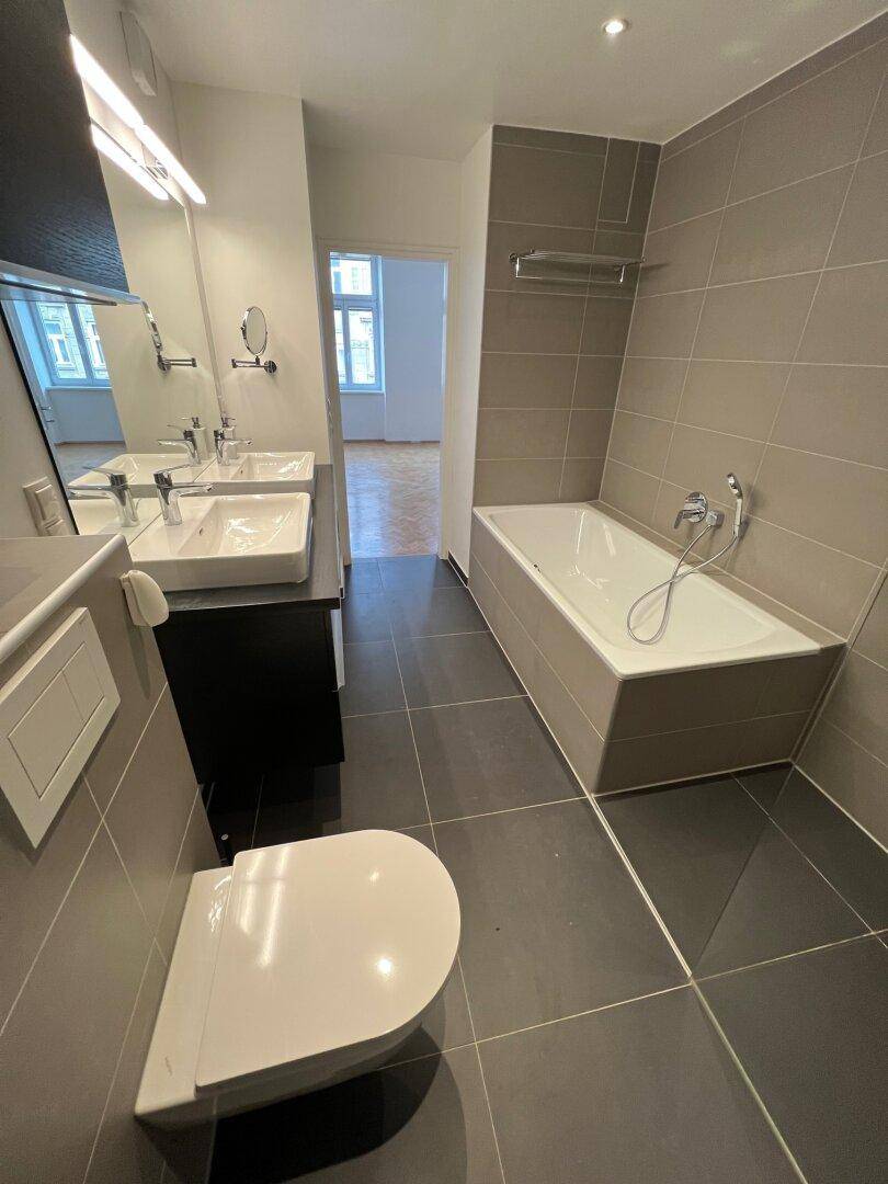 Modernes Badezimmer mit Badewanne, Doppelwaschbecken und einem wandhängenden WC.