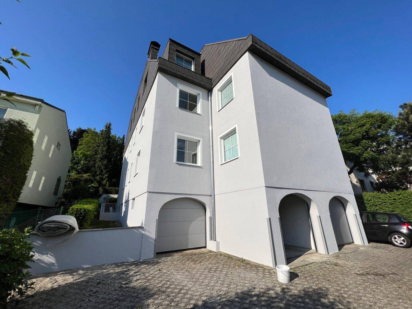 Vorderansicht des Hauses mit Garagentor und überdachten Parkplätzen.