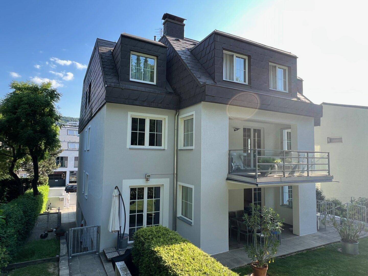 Seitenansicht des Hauses mit Balkon, Terrasse und gepflegter Hecke im Garten.