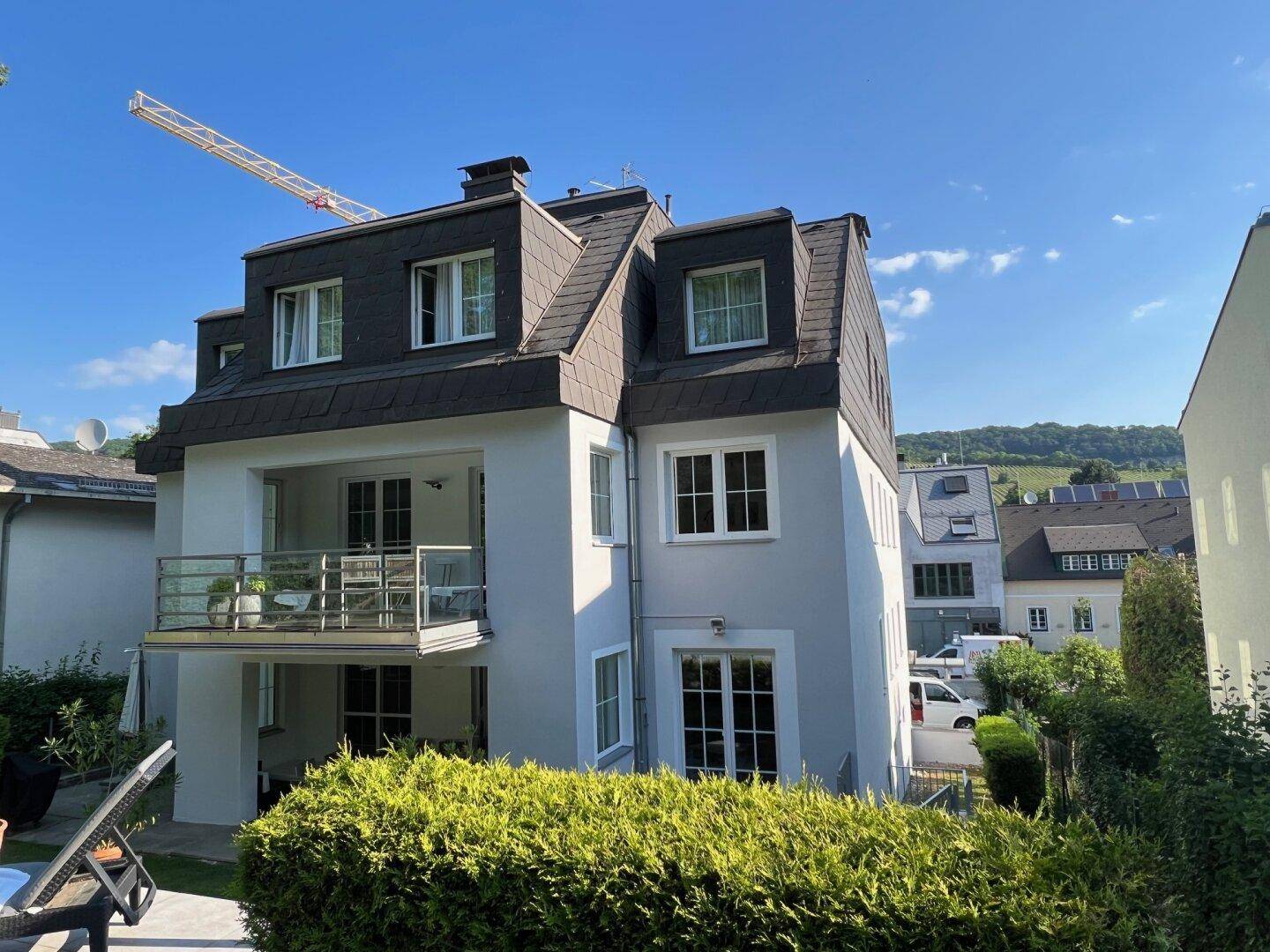 Rückansicht des Hauses mit Balkon und Mansarddach unter blauem Himmel.