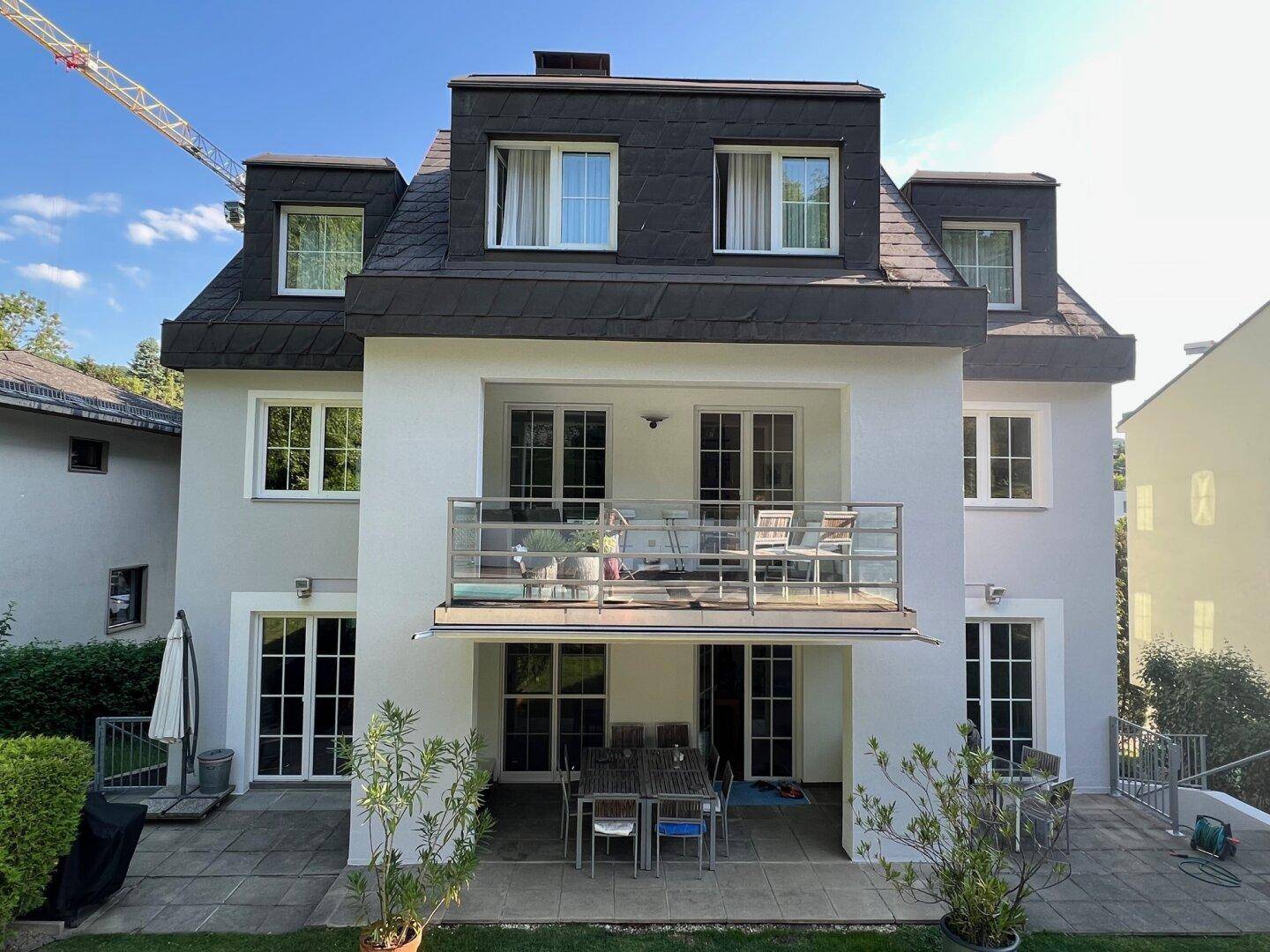 Rückseite des Hauses mit Balkon und einer möblierten Terrasse im Erdgeschoss.