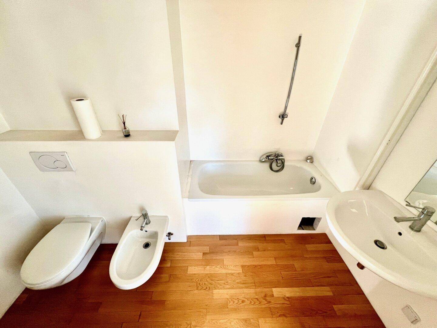Badezimmer mit Badewanne, Bidet, Toilette und Parkettboden.