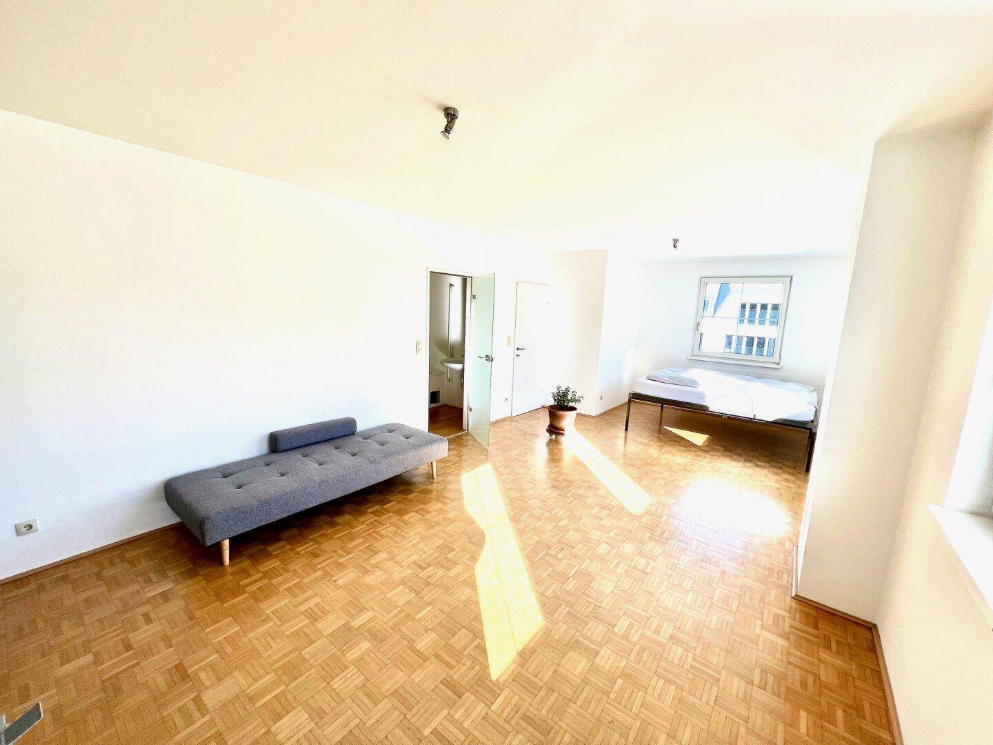 Helles Schlafzimmer mit Parkettboden, Tagesbett und Zugang zum Badezimmer.