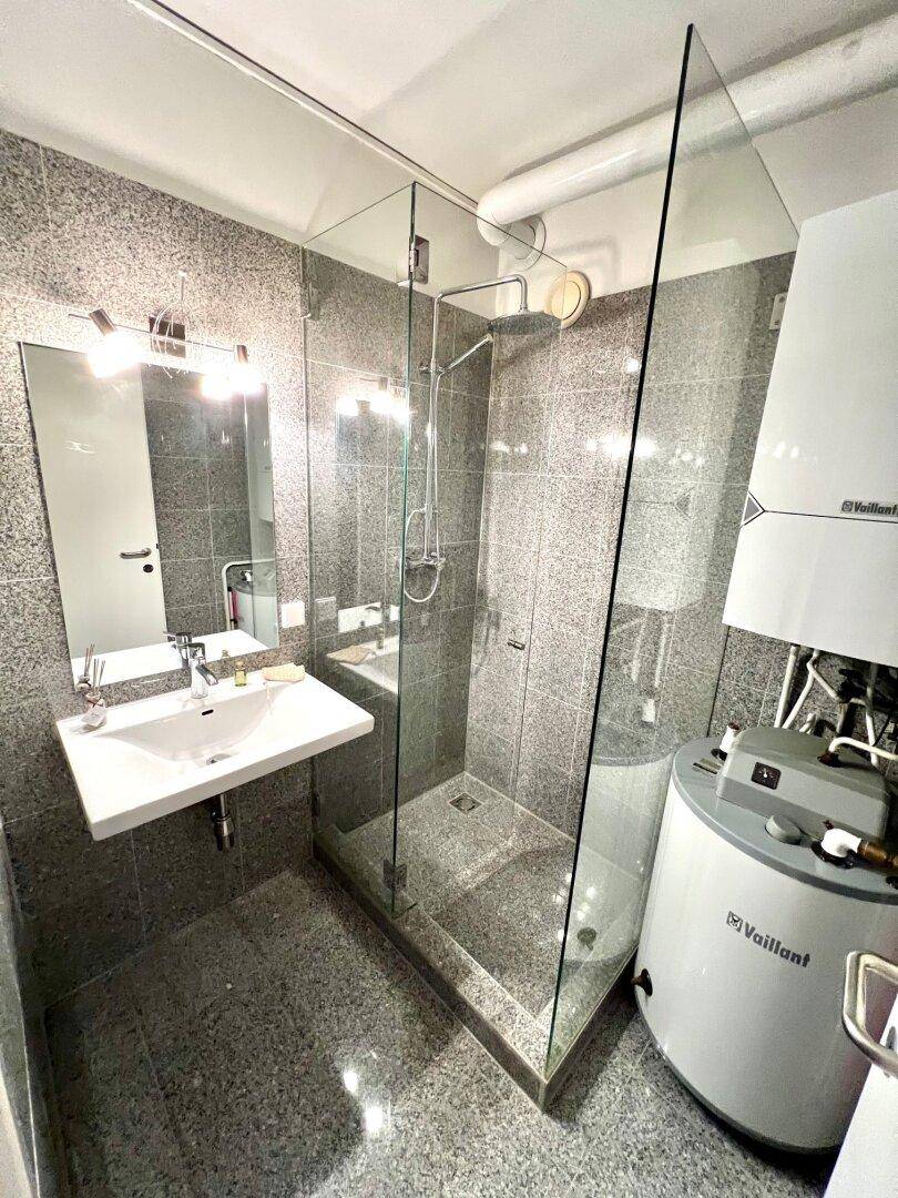 Modernes Badezimmer mit Duschkabine, Waschbecken und grauen Fliesen.