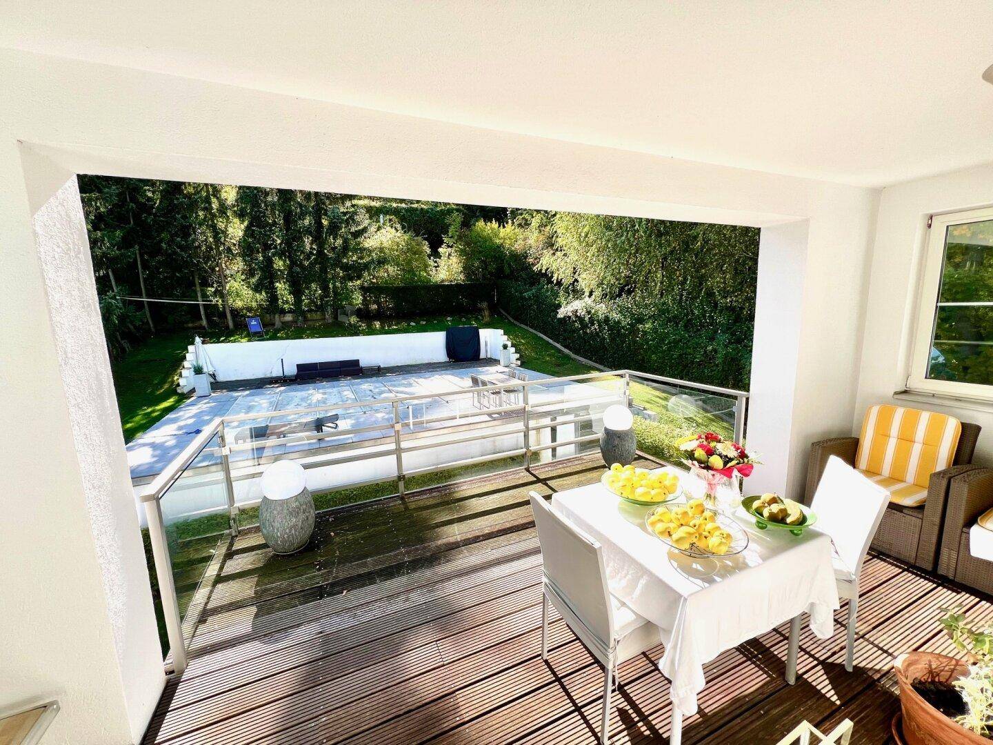 Überdachte Loggia mit Holzboden, Esstisch und Blick auf den Poolbereich.