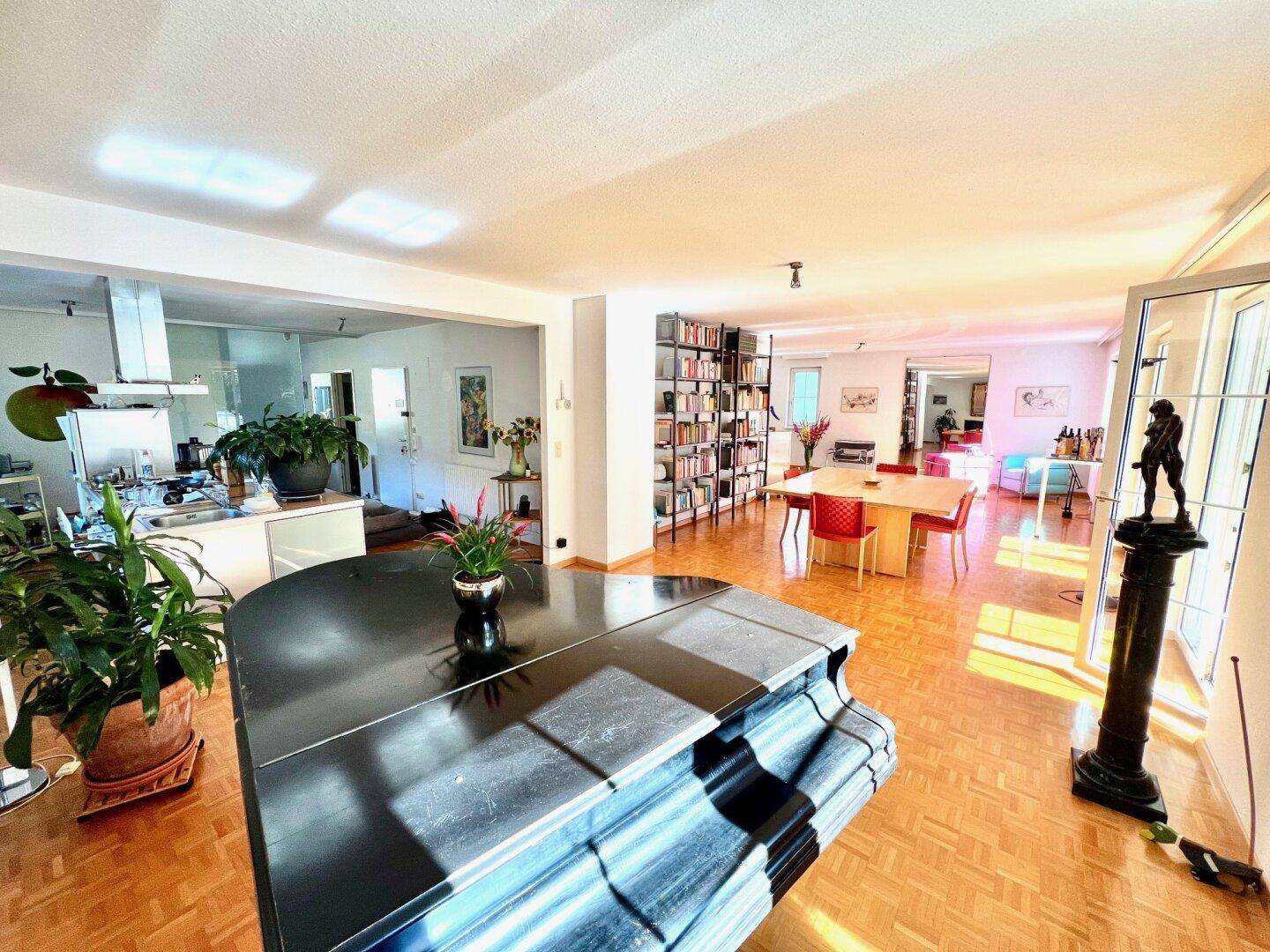 Offener Wohnbereich mit Klavier, Parkettboden und Blick in die moderne Küche.