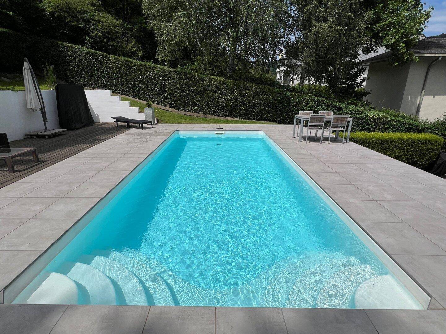 Moderner Swimmingpool im Gartenbereich mit breiter Treppe und Fliesenumrandung.