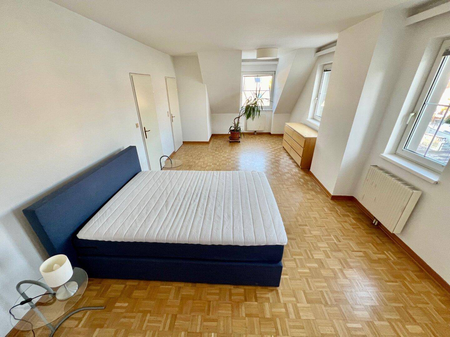 Helles Schlafzimmer im Dachgeschoss mit Parkettboden und schrägen Wänden.