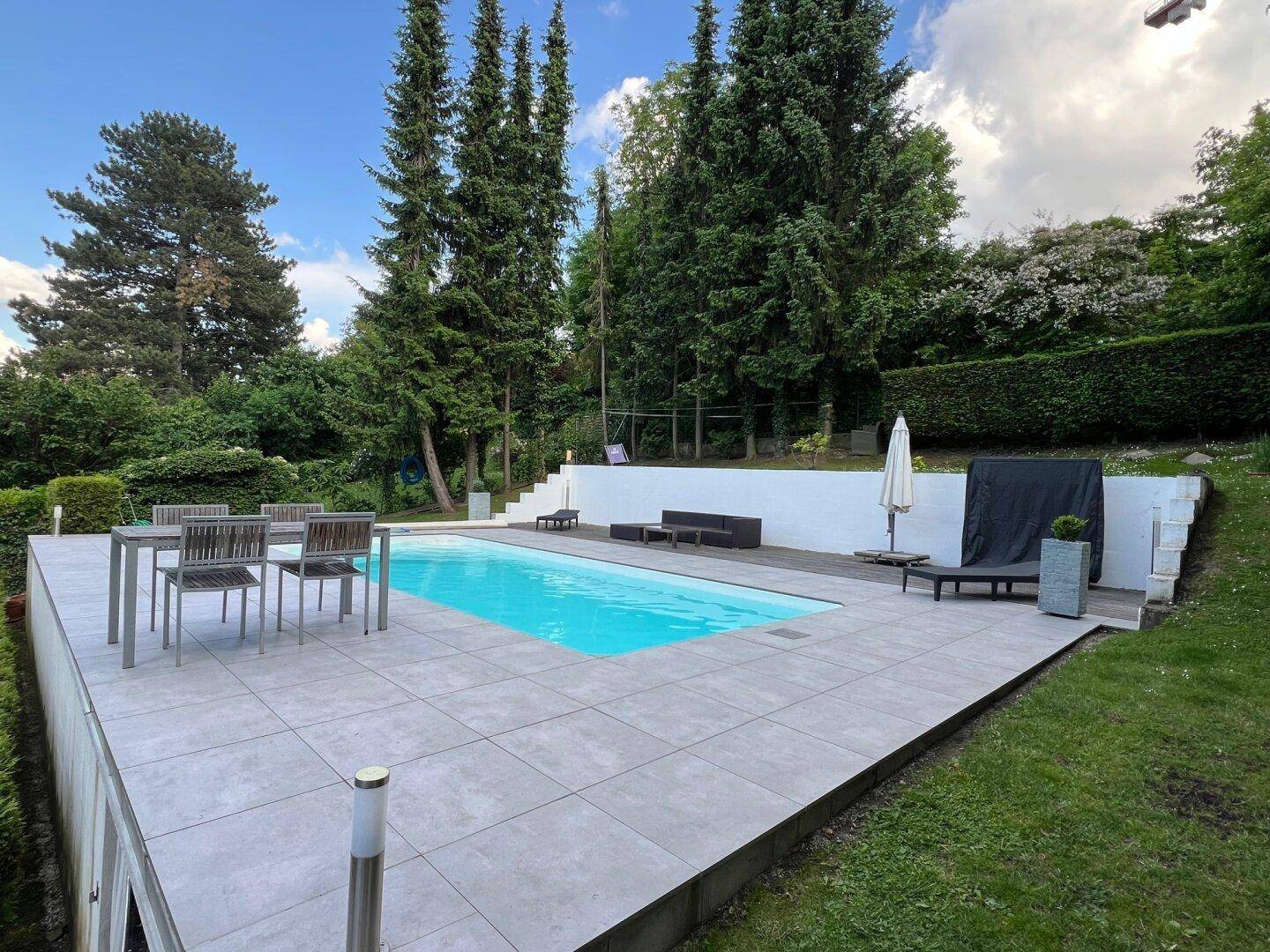 Gepflegter Garten mit Swimmingpool, Essbereich und hohen Bäumen.