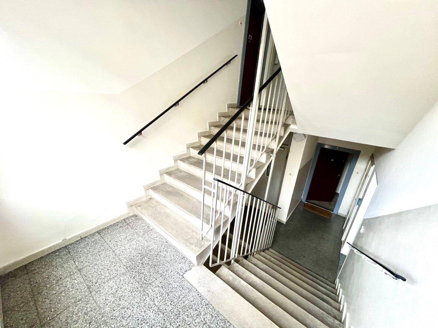 Heller Treppenaufgang mit Steinstufen und Metallgeländer in einem Mehrfamilienhaus.