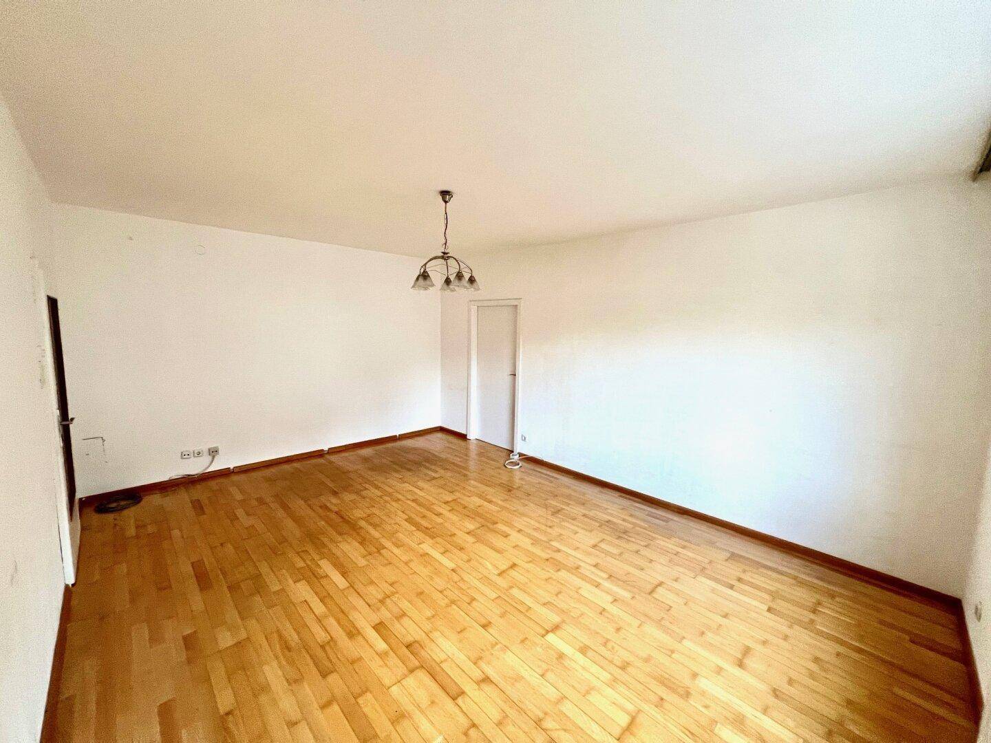 Leeres Zimmer mit Parkettboden und weißen Wänden, bereit für die individuelle Gestaltung.