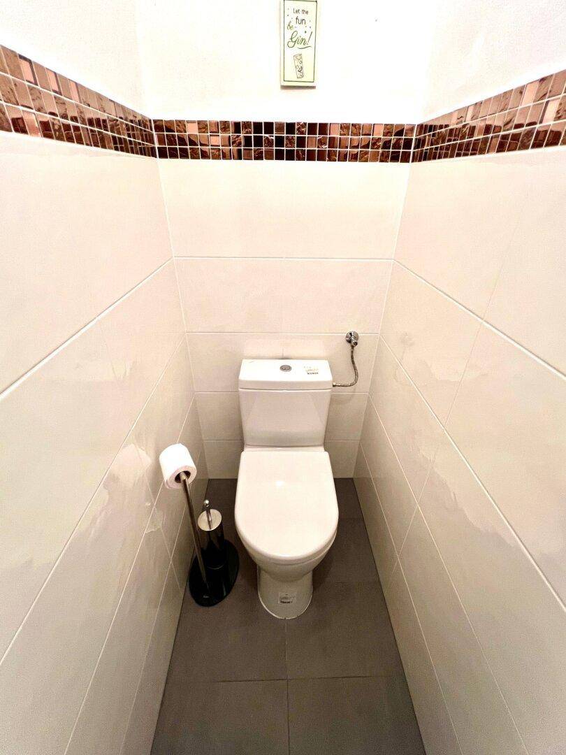 Modern geflieste Gästetoilette mit Wand-WC und dekorativem Fliesenband.