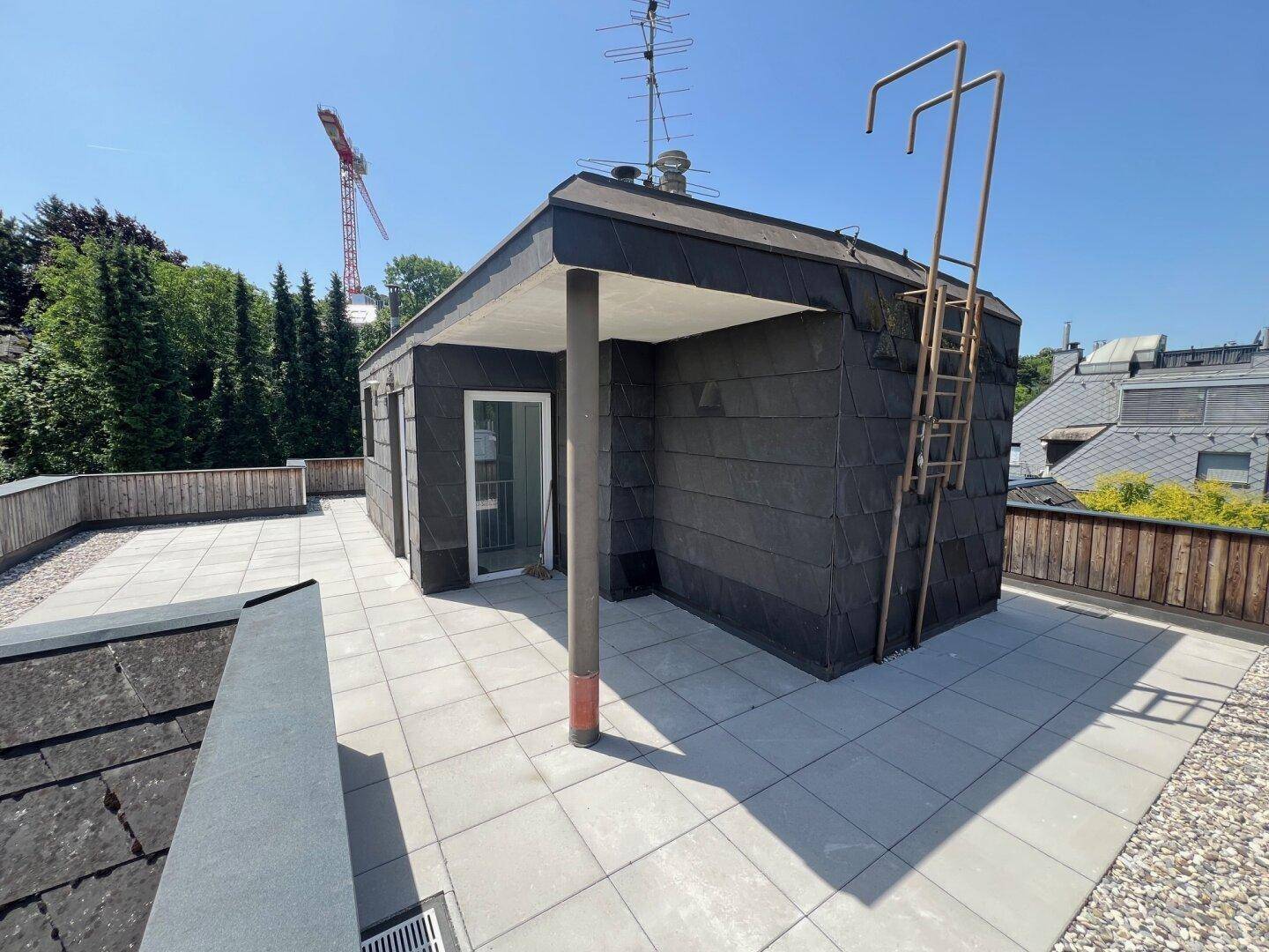 Weitläufige Dachterrasse mit Zugang zu einem kleinen Gebäude und Panoramablick.
