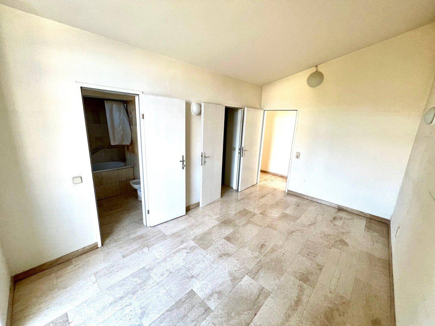 Schlafzimmer mit Marmorboden und mehreren Türen, die zu angrenzenden Räumen führen.