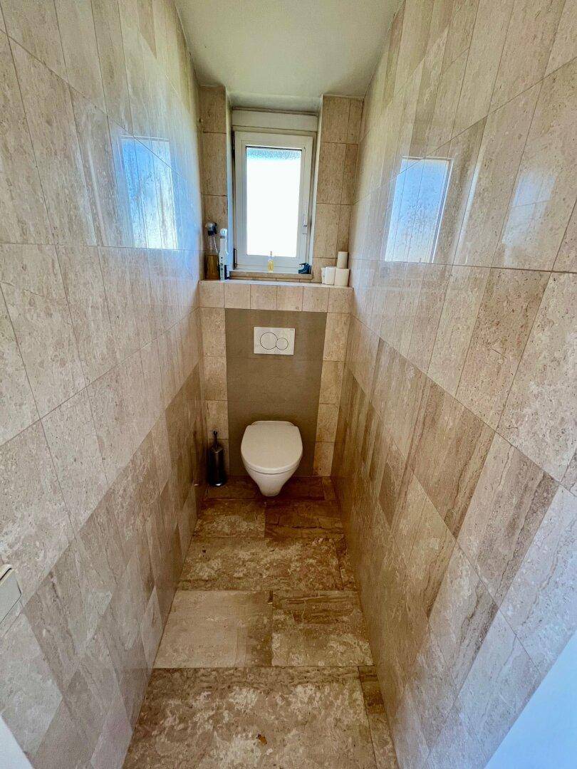 Separate Toilette mit Wand-WC und Fliesen an Wänden und Boden.