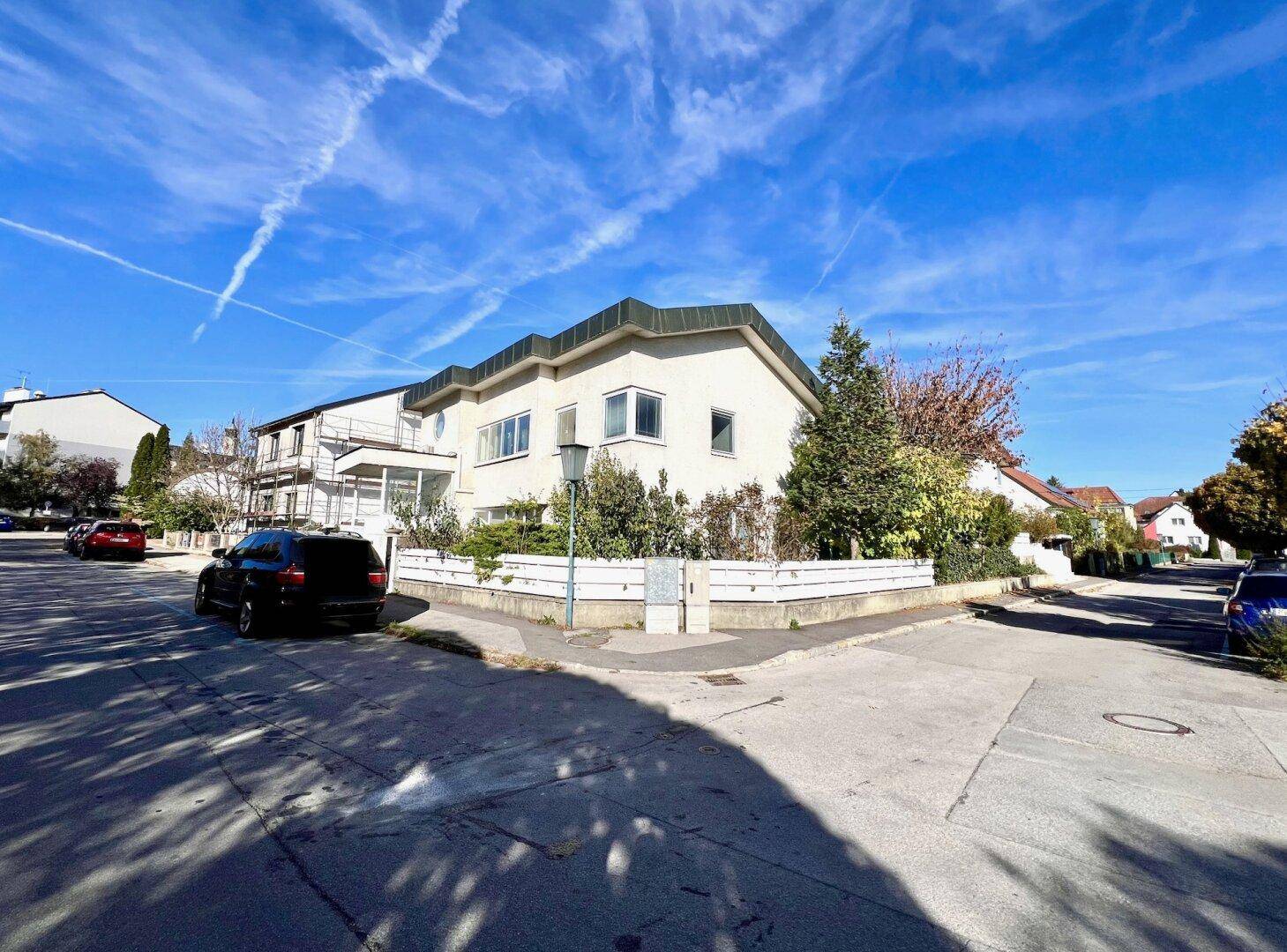 Wohnhaus an einer Straßenecke mit gepflegter Umgebung unter blauem Himmel.