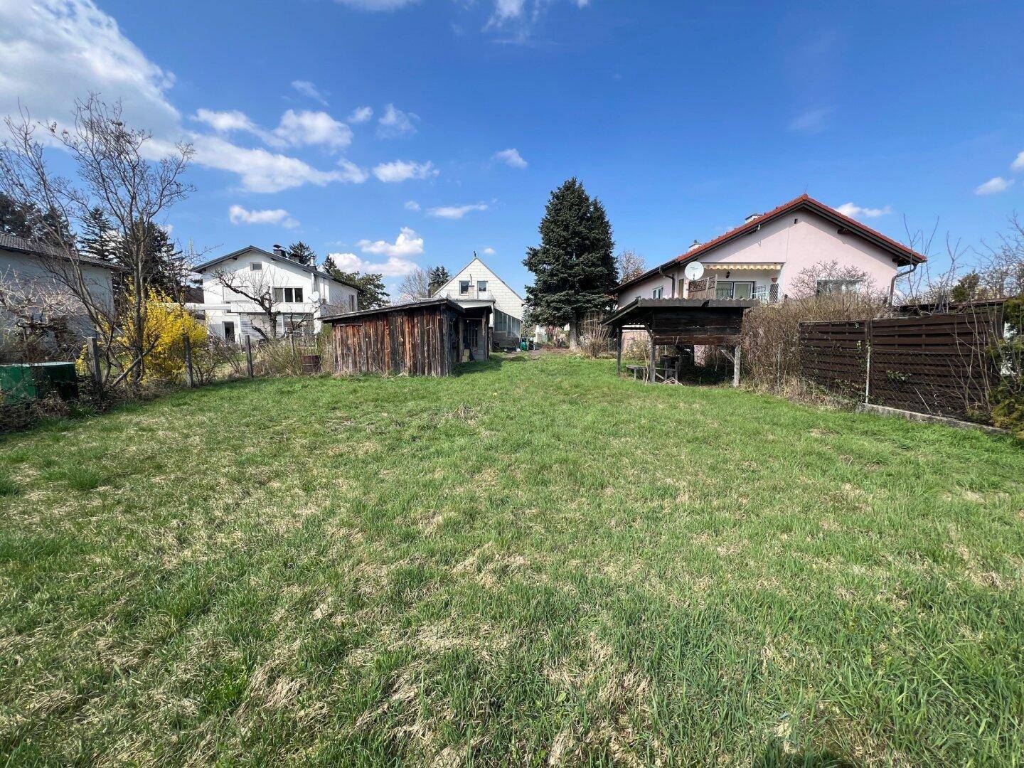 Großer, sonniger Gartenbereich mit Rasenfläche und alten Schuppen, umgeben von weiteren Wohnhäusern.