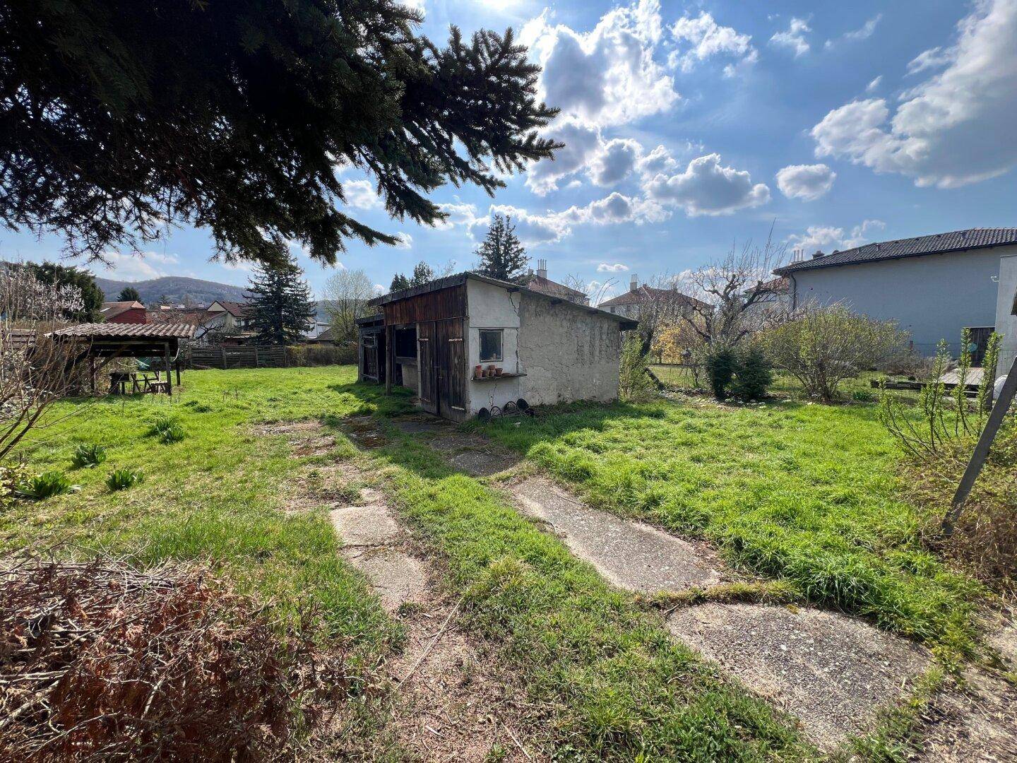 Unbefestigter Weg führt durch den grünen Garten zu einem alten Schuppen unter sonnigem Himmel.